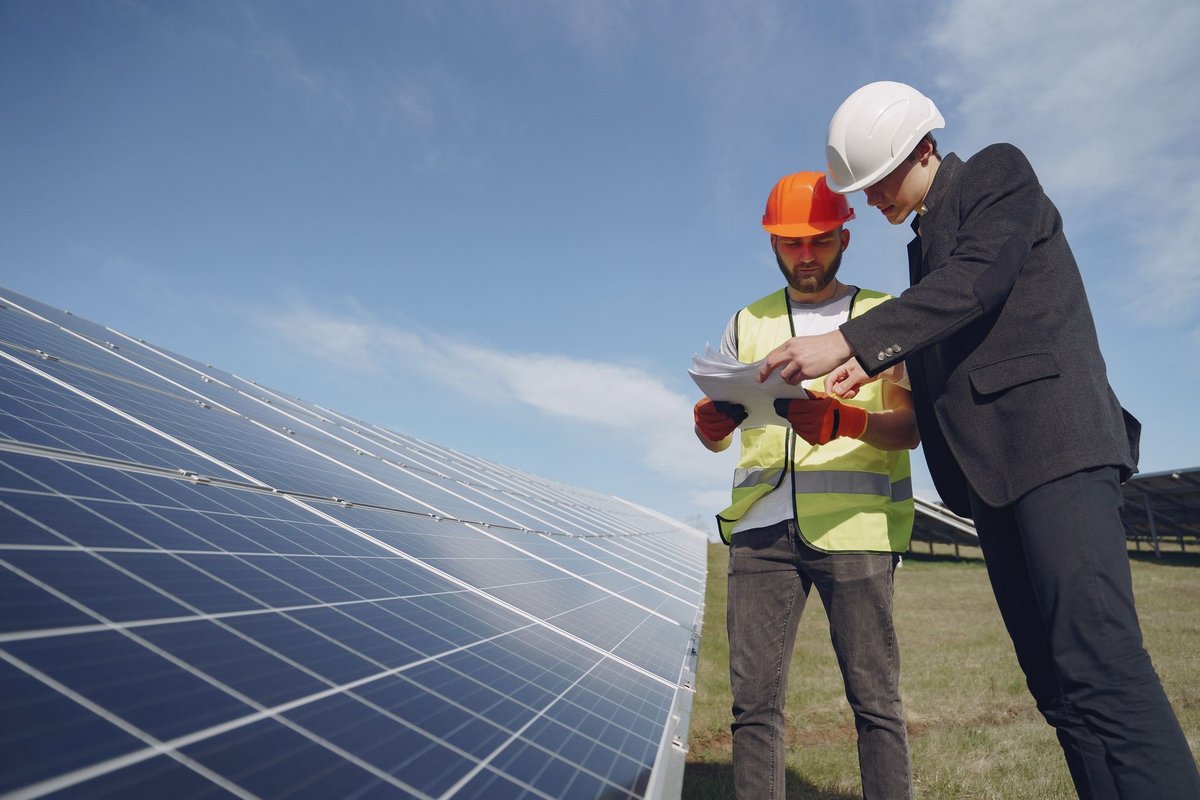 Commercial solar technician in hard hat and safety vest reviewing paperwork beside a rooftop solar array