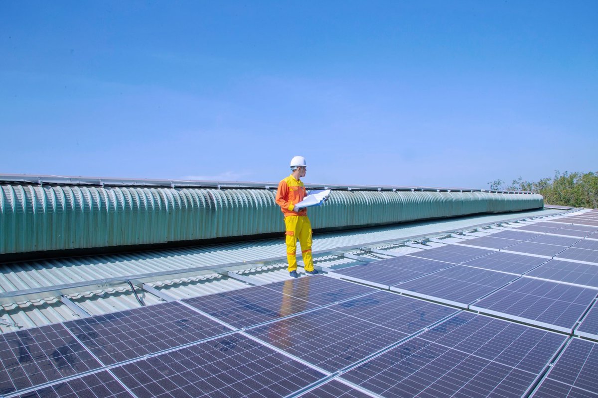 Commercial solar installer with clipboard inspecting a rooftop photovoltaic array in bright daylight