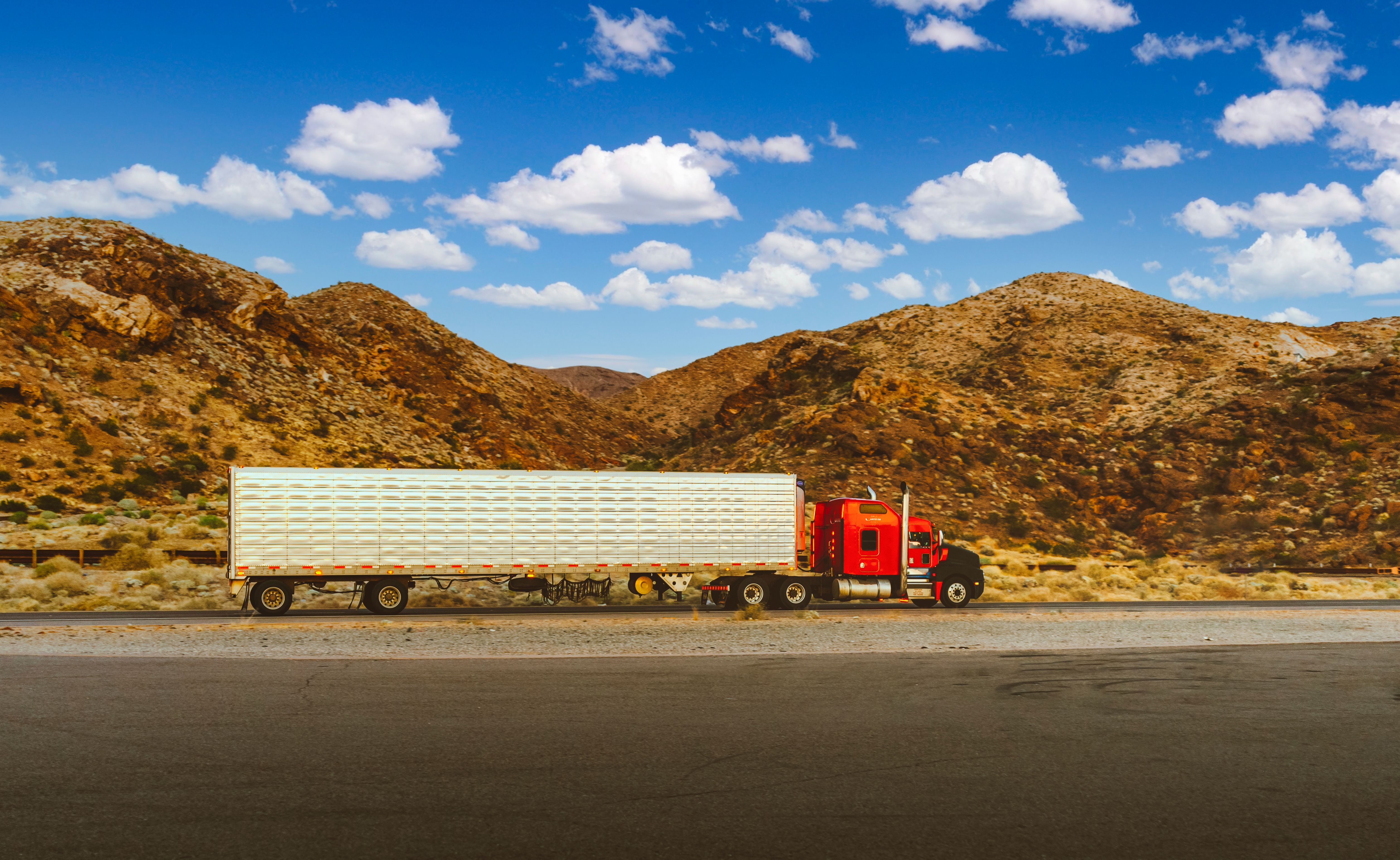 Red semi-truck with trailer driving on a desert highway