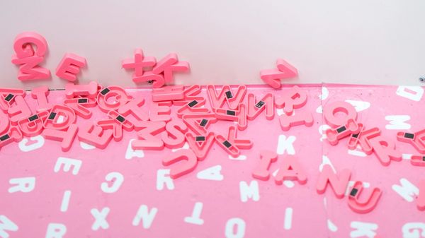 Pink letter magnets jumbled up on a pink and white background.