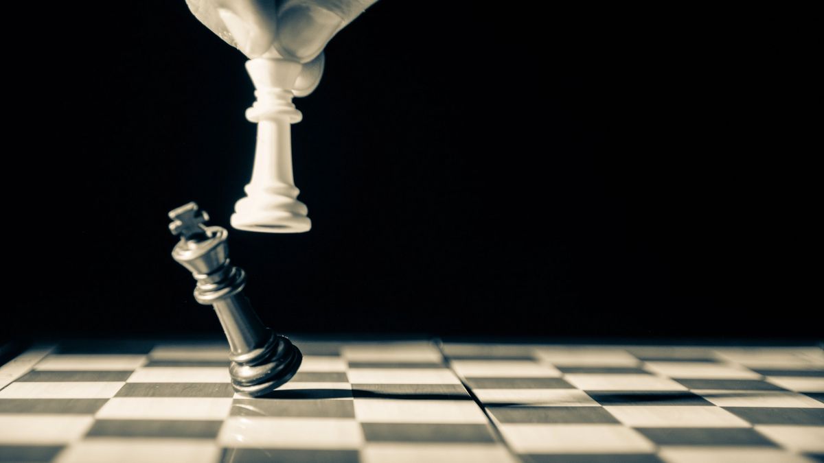 Close up of white king taking down black king. Hand and fingers and chess board with vintage look