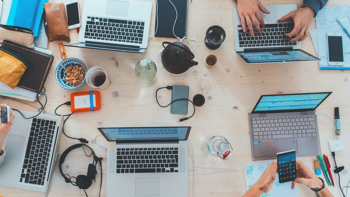 Laptops, electronics and coffee cups on a table top.