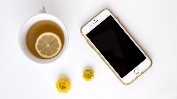 Iphone and lemon tea on a table with yellow flowerheads.
