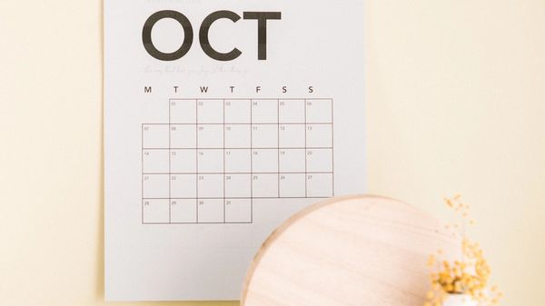 An October wall calendar, a white vase and an open book.