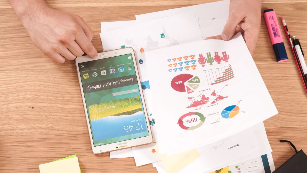 Hands looking at charts and a tablet on a desk.