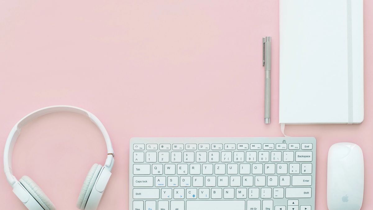 Headphones, notebook, pen, keyboard and mouse on a pink background.