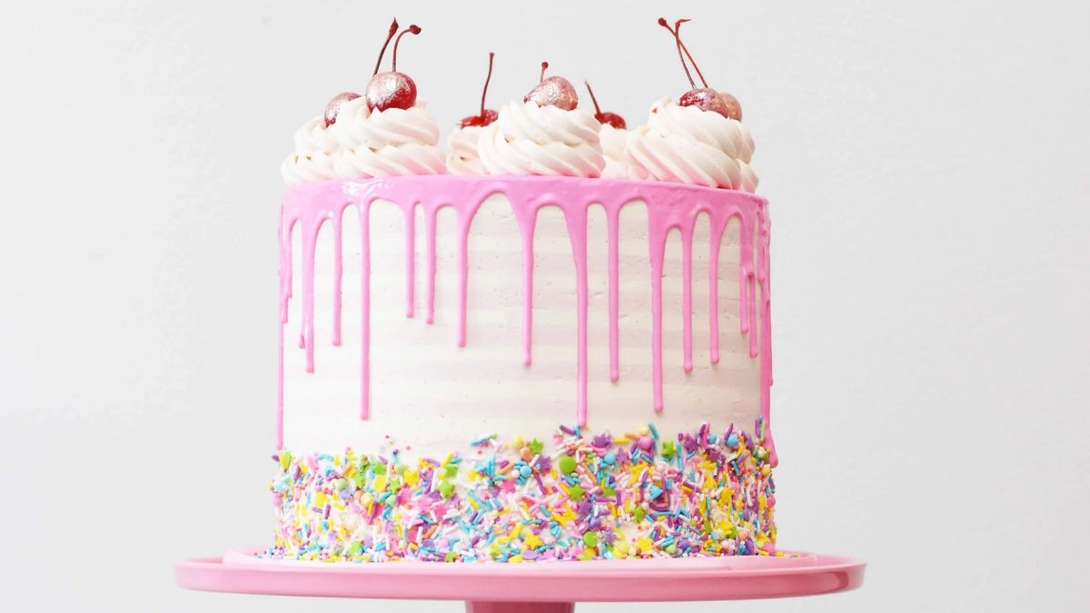 A really delicious pink birthday cake with cream and cherries on top and sprinkles!