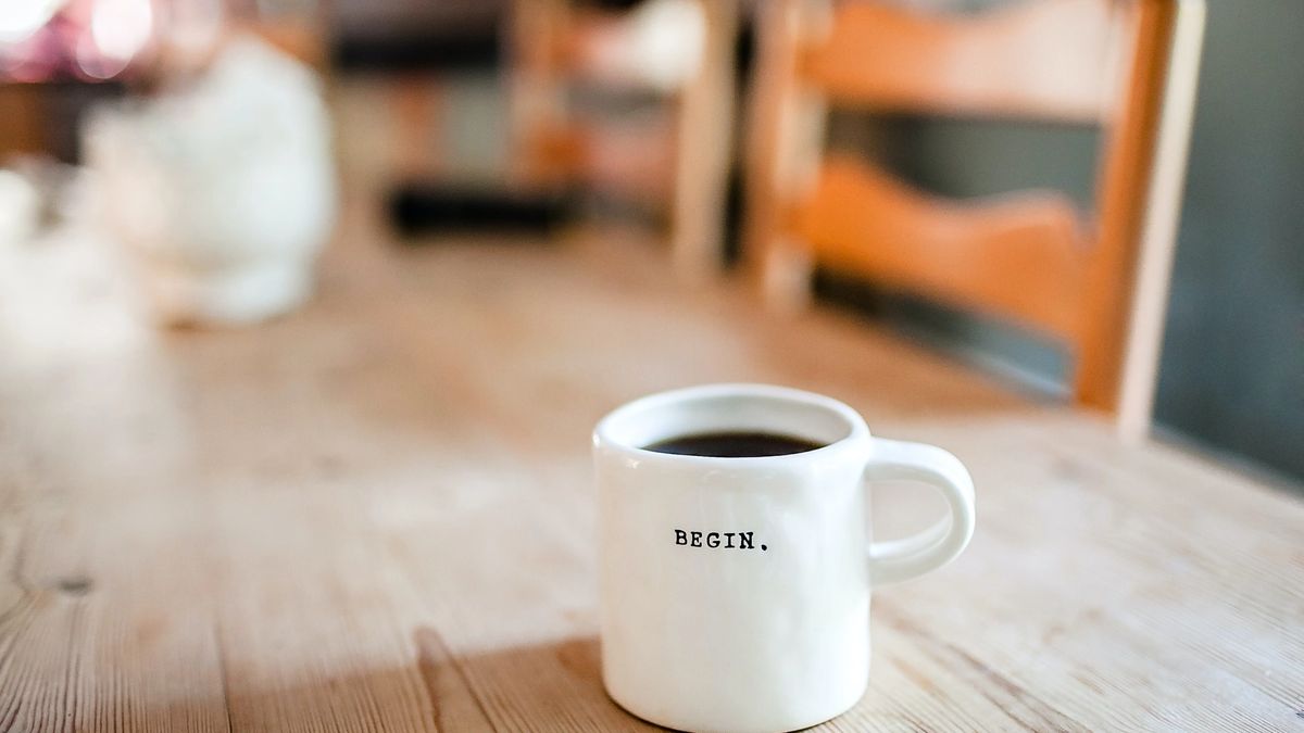 A mug with the word "Begin" imprinted in it on a wooden table.