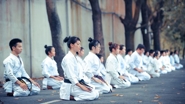 Martial arts practitioners in lines, knelt down with eyes closed.