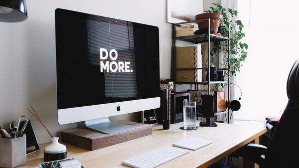 Home office space containing a Mac that contains the words "do more".