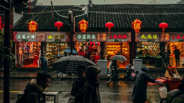 People walking past shops in Shanghai in the rain at dusk.
