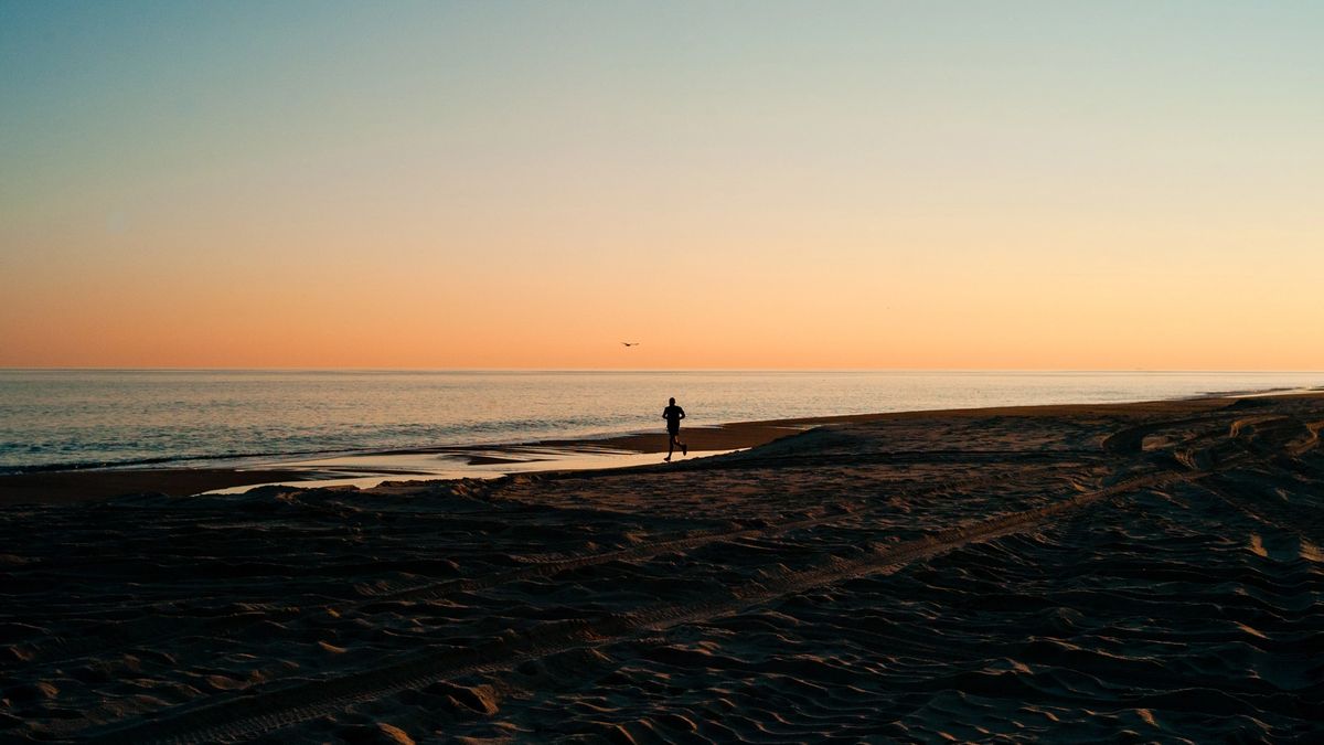 Silhouette of a runner on a beach at sunset.