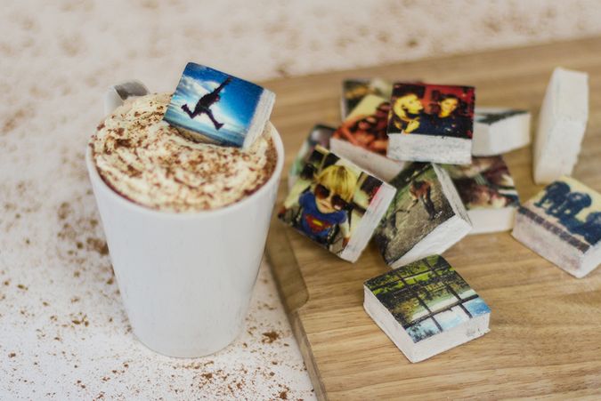 Mug of hot chocolate with boomf printed photo marshmallows on a wooden chopping board.