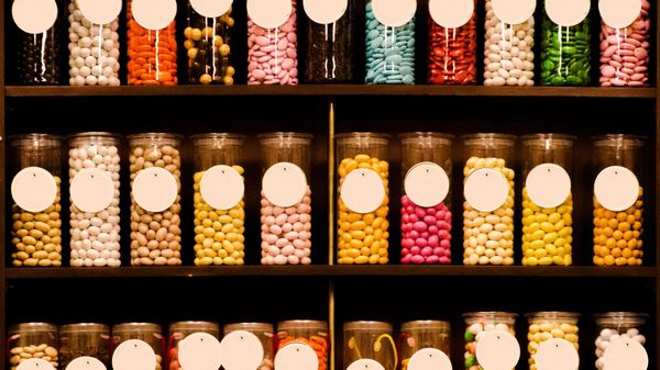Lots of multicoloured sweets in glass jars on a shelf.