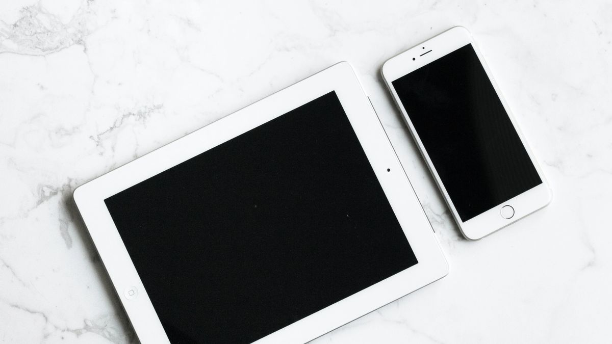 White tablet and smartphone on a white marble surface.