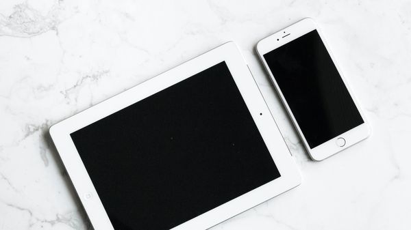 White tablet and smartphone on a white marble surface.