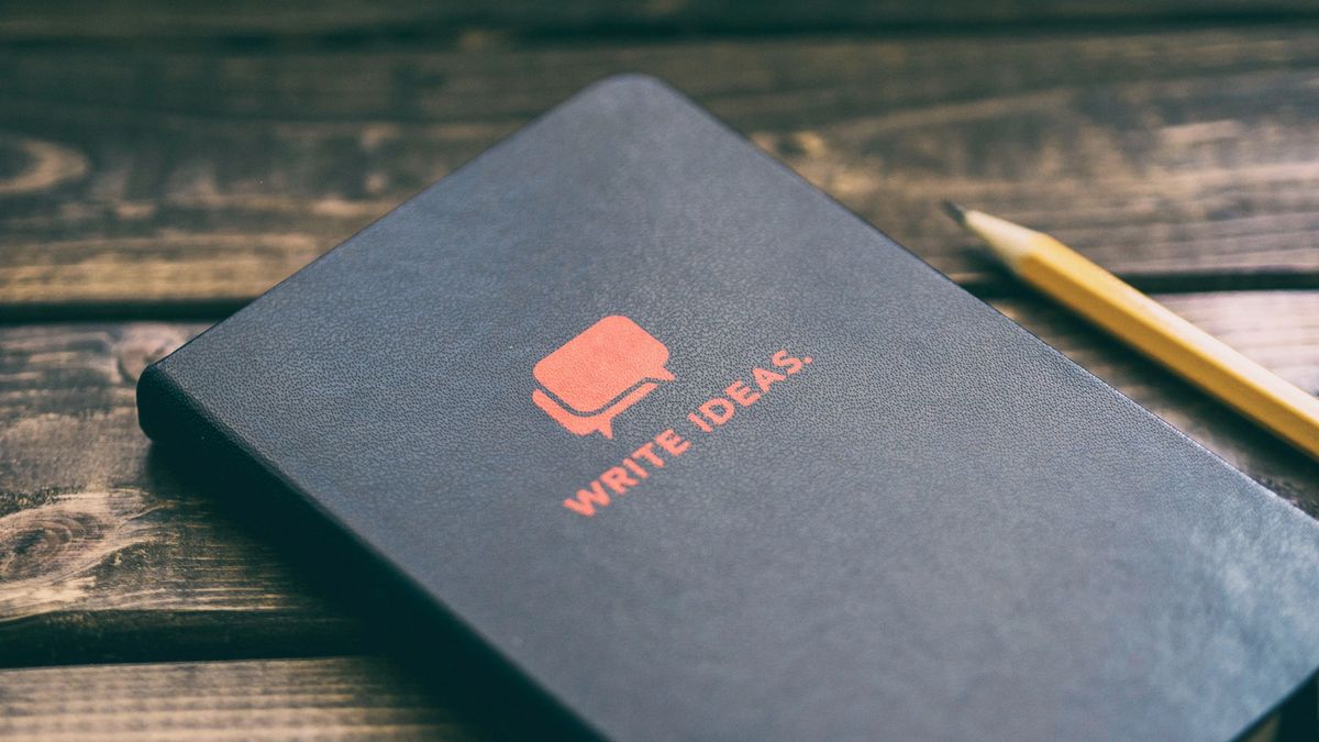 Closed notebook with the words "write ideas" and a pencil on a wooden table.