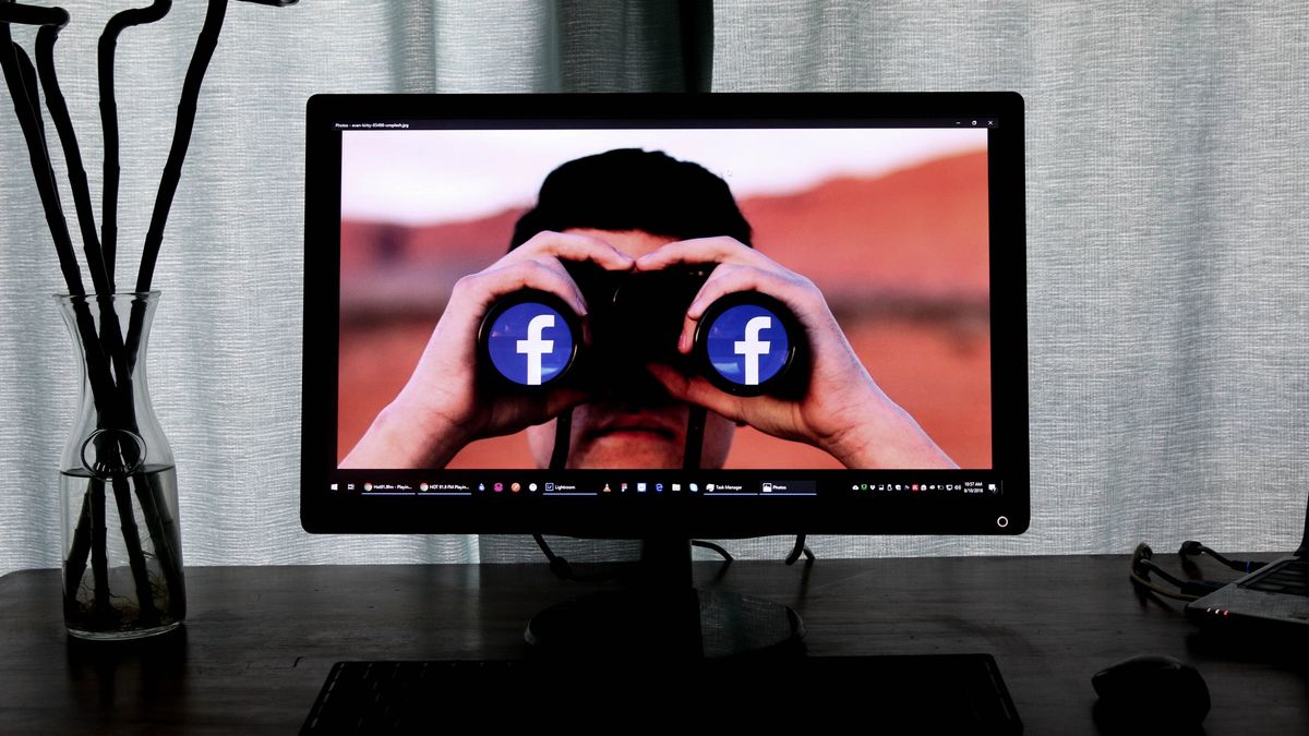 Monitor showing a photo of a person looking through a pair of binoculars, but each lens is a Facebook icon.