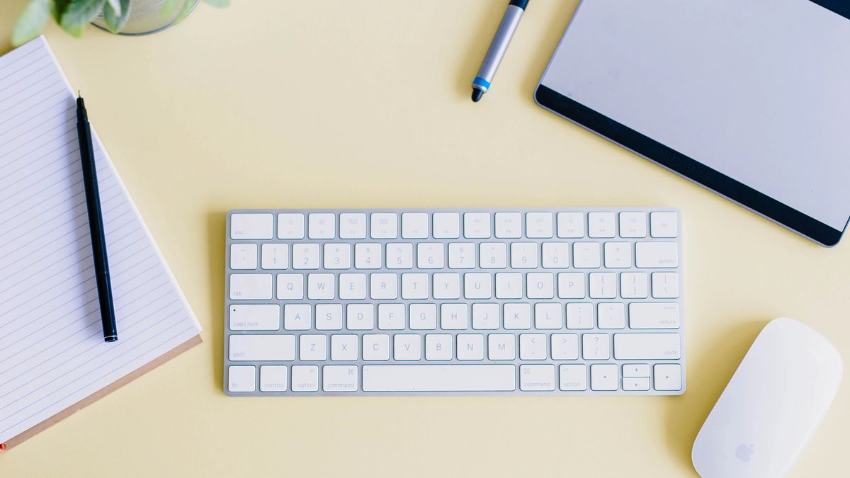 Apple keyboard, mouse and various notepaper on a yellow desk.