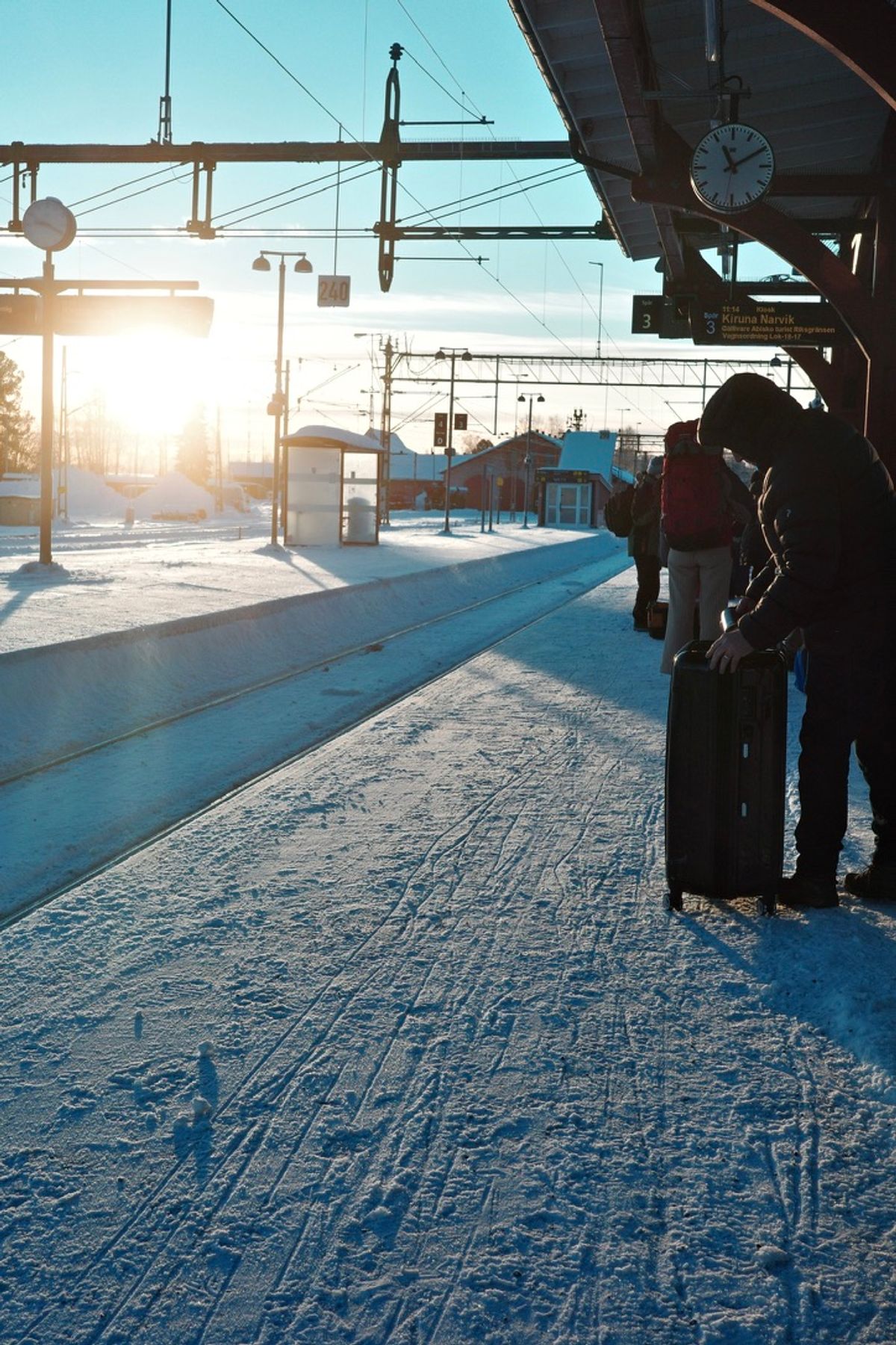 Travelers waiting on a snowy railway platform in morning light