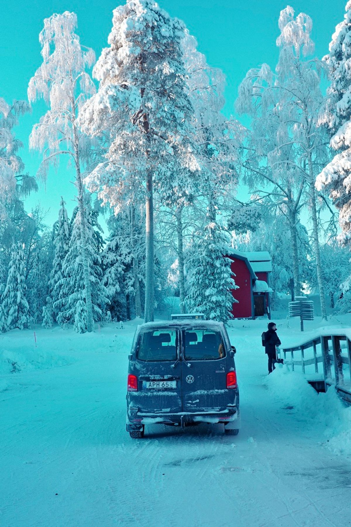 A van beneath snow-covered trees near a small red building
