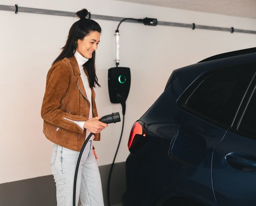 Foto av en kvinne som står med ladekabel foran bilen sin i borettslagets garasjeanlegg
