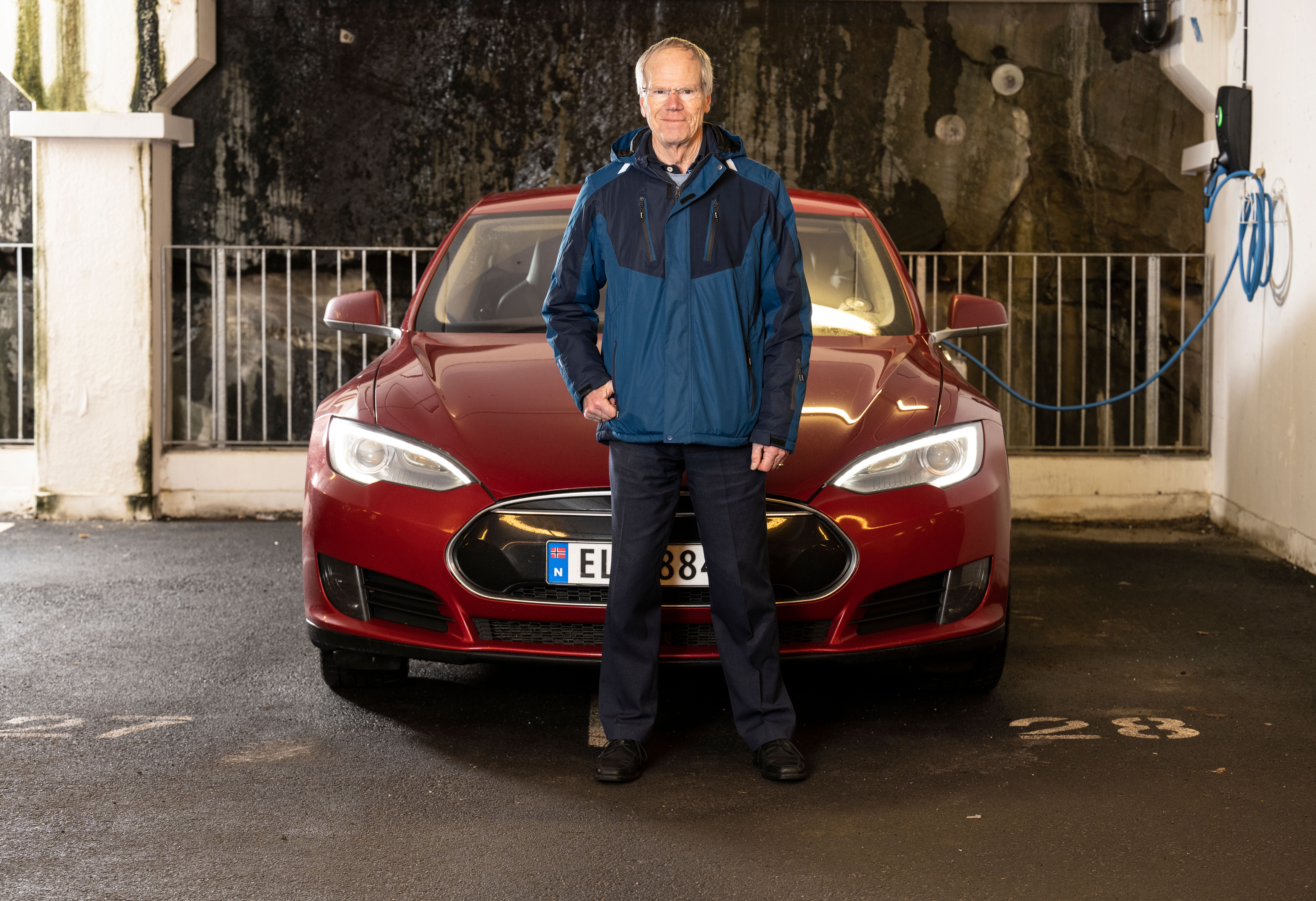 Mann foran rød elbil som lader i borettslagets garasje