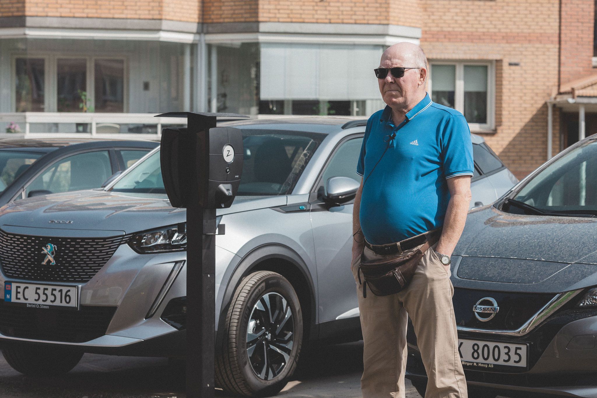 Bilde av en mann på en parkeringsplass mellom 2 elbiler som står foran en ladeboks for elbiler