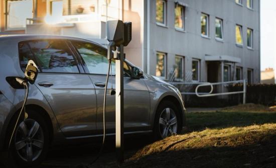 Bilde av en elbil som lader utenfor et leilighetskompleks. Bilen er koblet til en ladeboks som står på en stolpe.