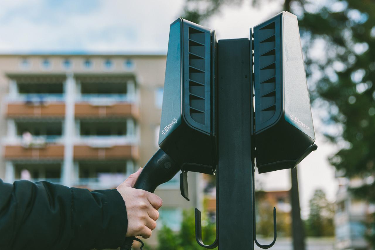 En person som holder på en ladekabel tilkoblet en utendørs ladeboks foran et leilighetskompleks