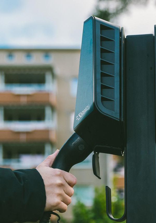 En hånd som holder på en ladekabel på en utendørs ladeboks for elbillading fra Elaway.