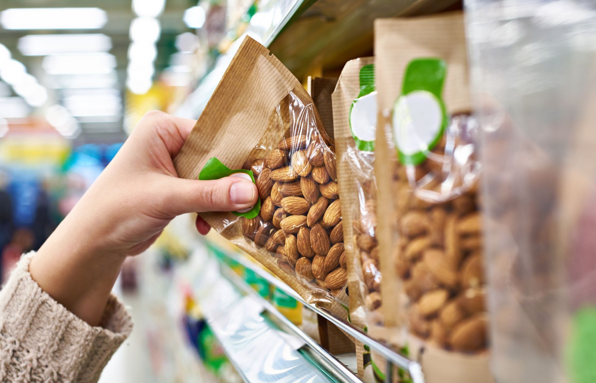 Hånd tager en pose mandler fra en butikshylde med flere emballerede fødevarer