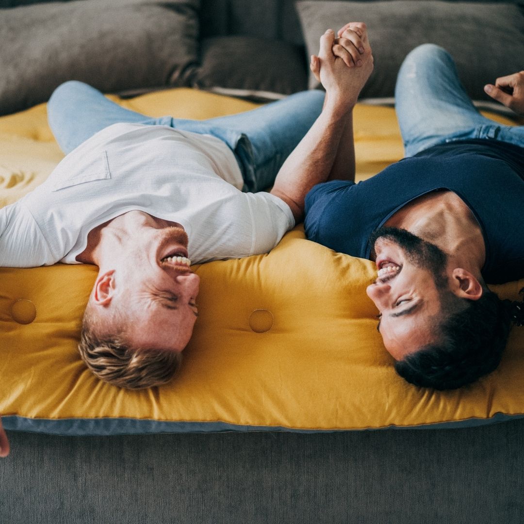 a gay couple holds hands while laughing and laying down on a date