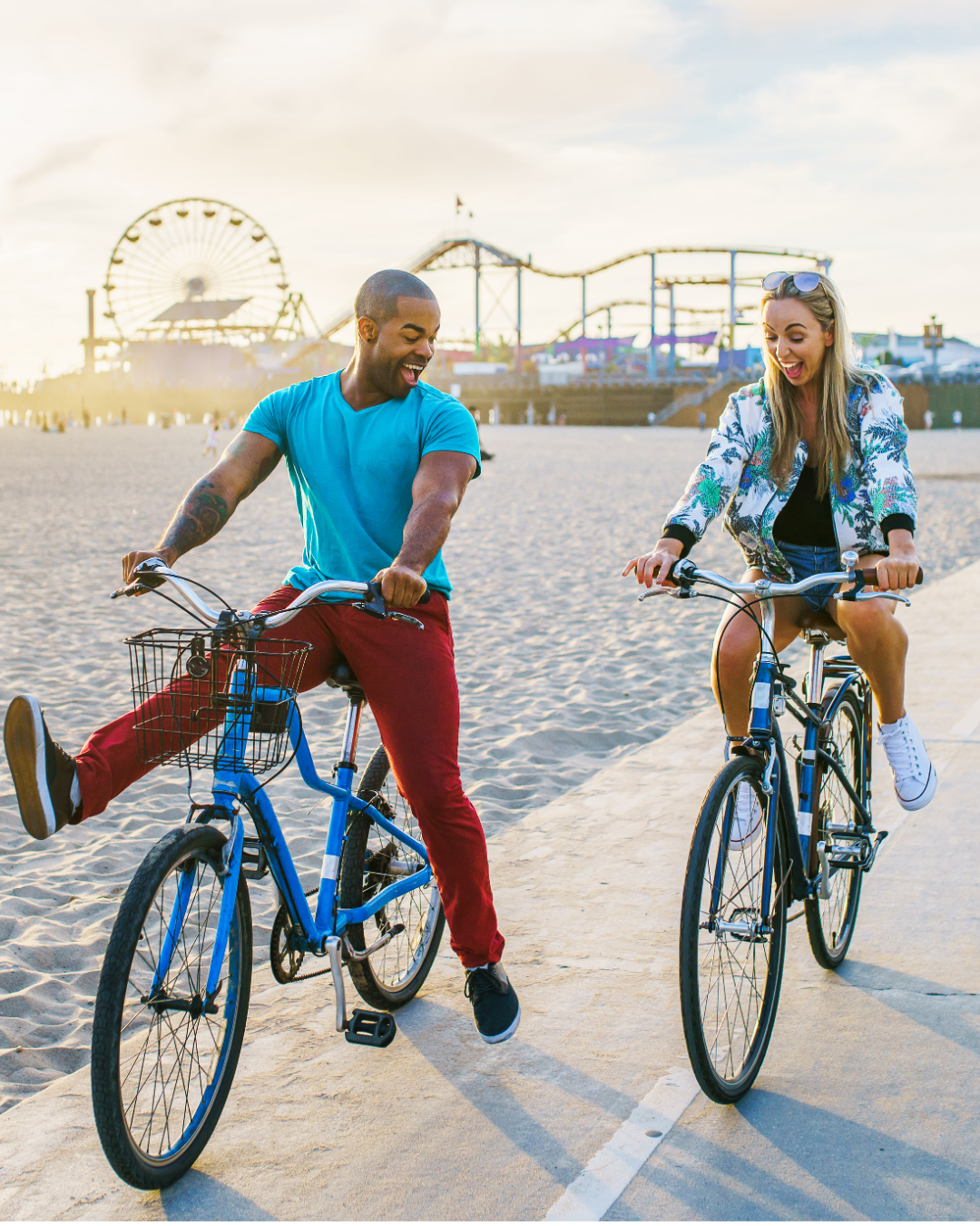 How to Ask someone out: Two people happily riding bicycles on a beach promenade with a ferris wheel in the background at sunset on a date