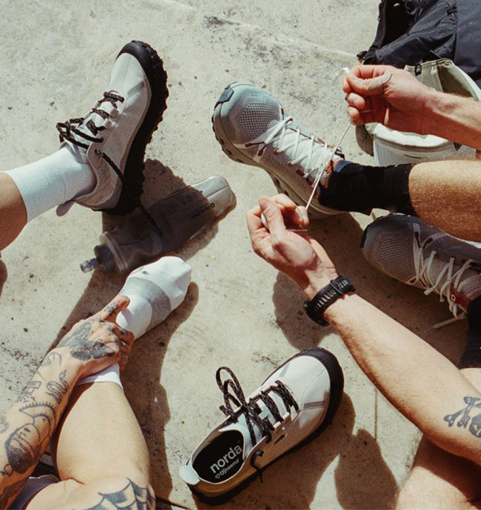 Hands lacing up grey trail sneakers on a concrete floor