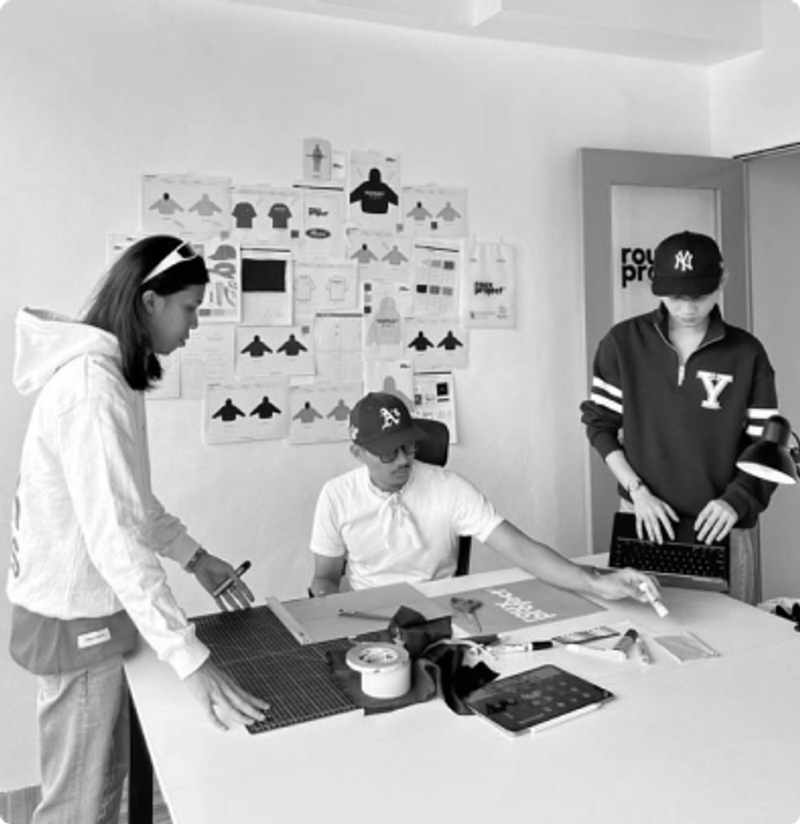 Three people working at a table in front of a mood board wall