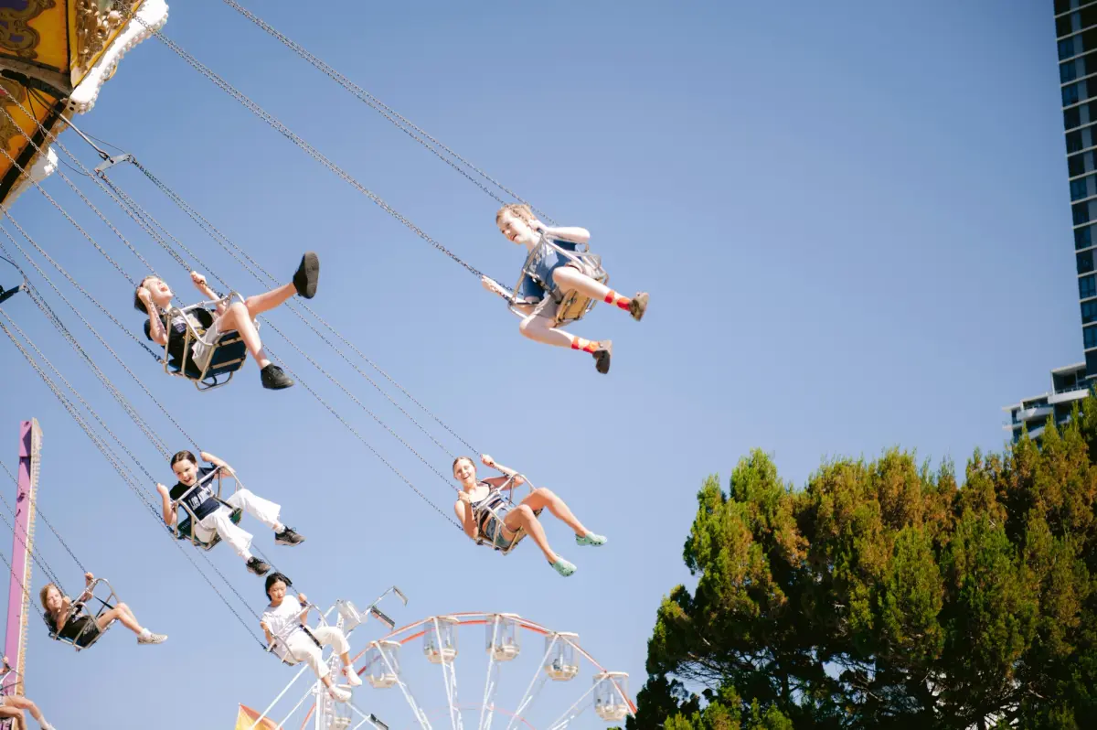 Children riding a swing carousel at an amusement park under a clear blue sky.