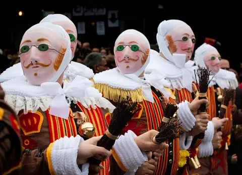 Gilles performers in traditional white costumes and wax masks at Binche Carnival in Belgium