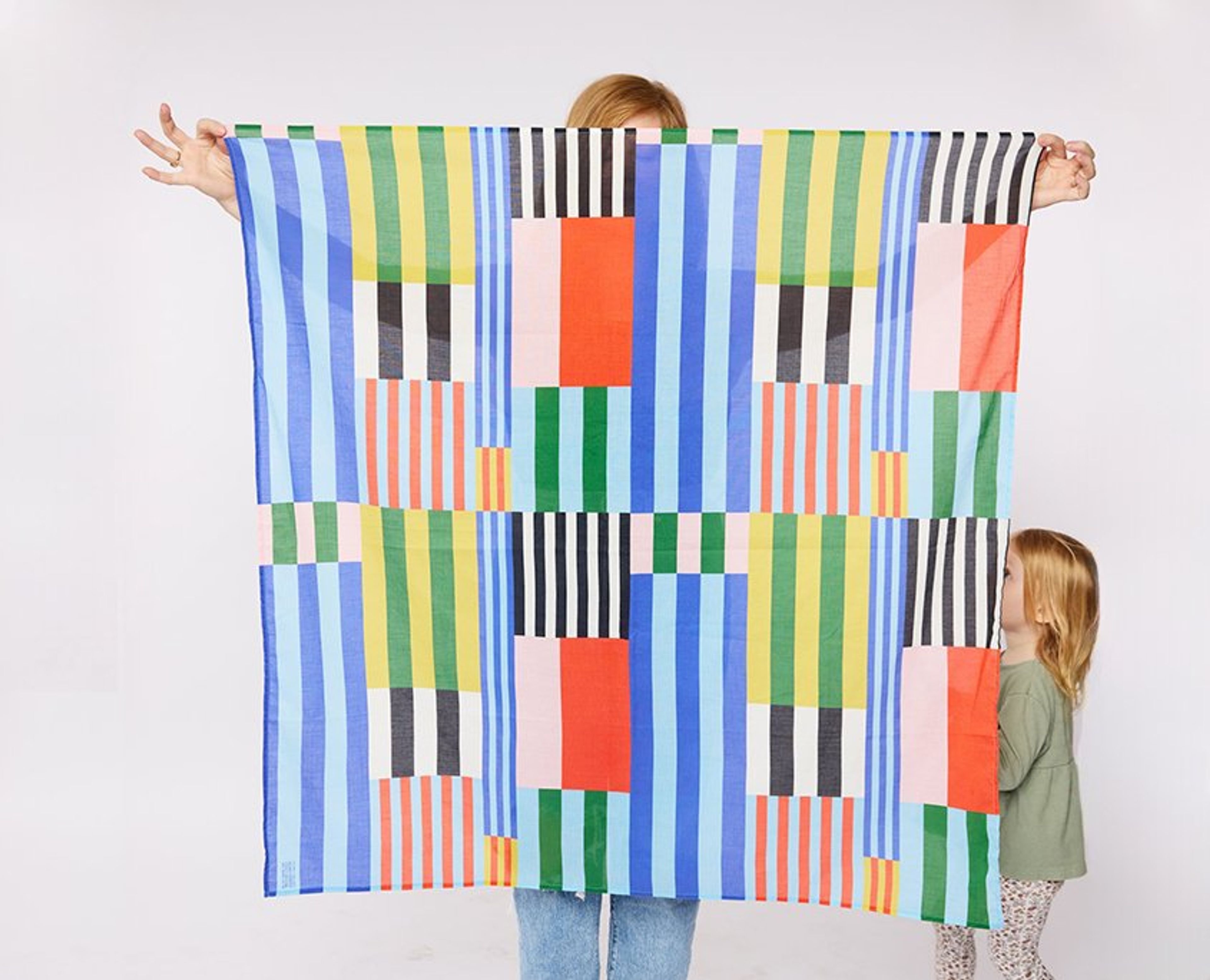 Adult and child holding a colorful striped patchwork blanket against white wall.