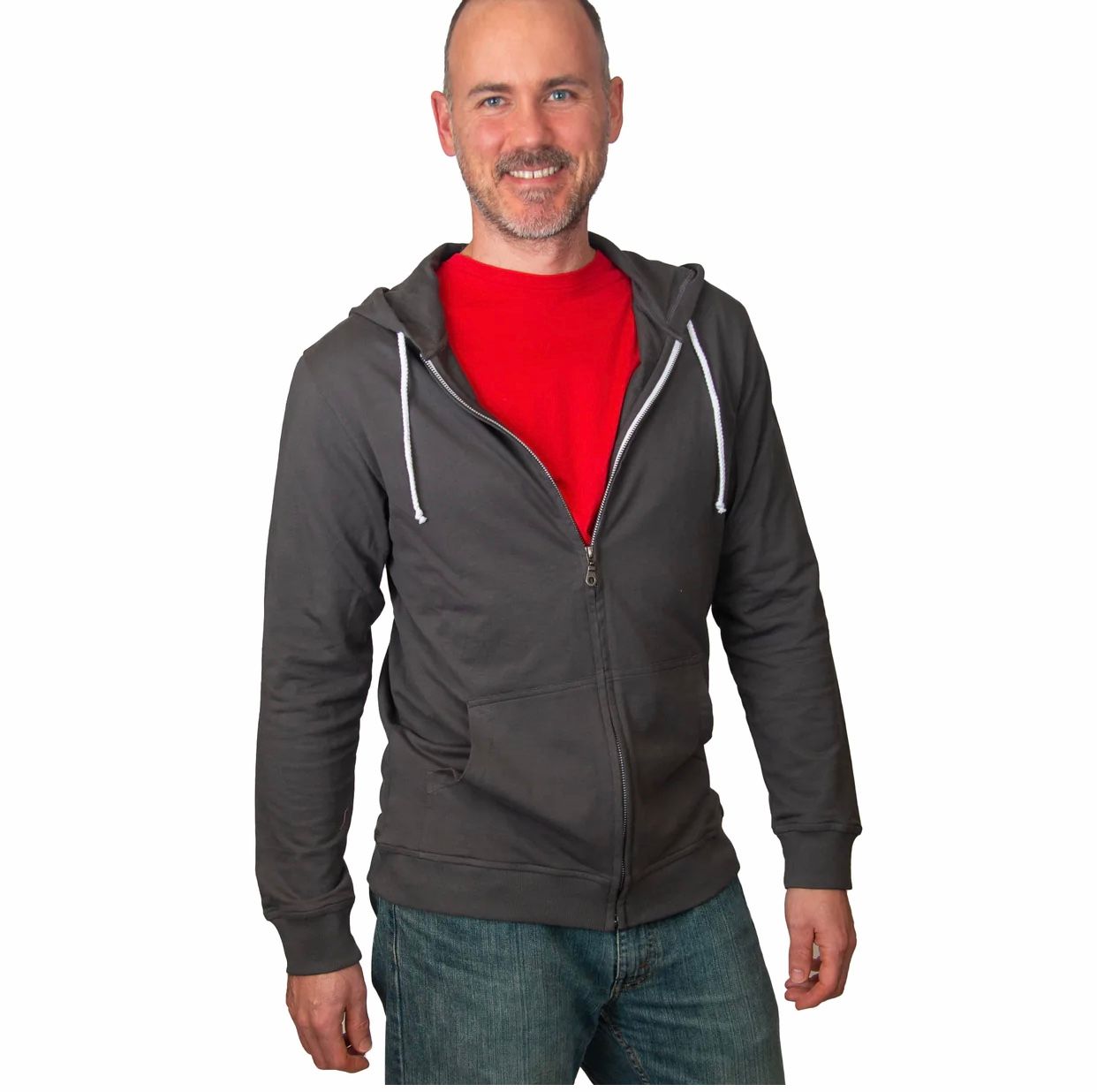 Man wearing red t-shirt and charcoal zip-up hoodie with jeans, smiling at camera.