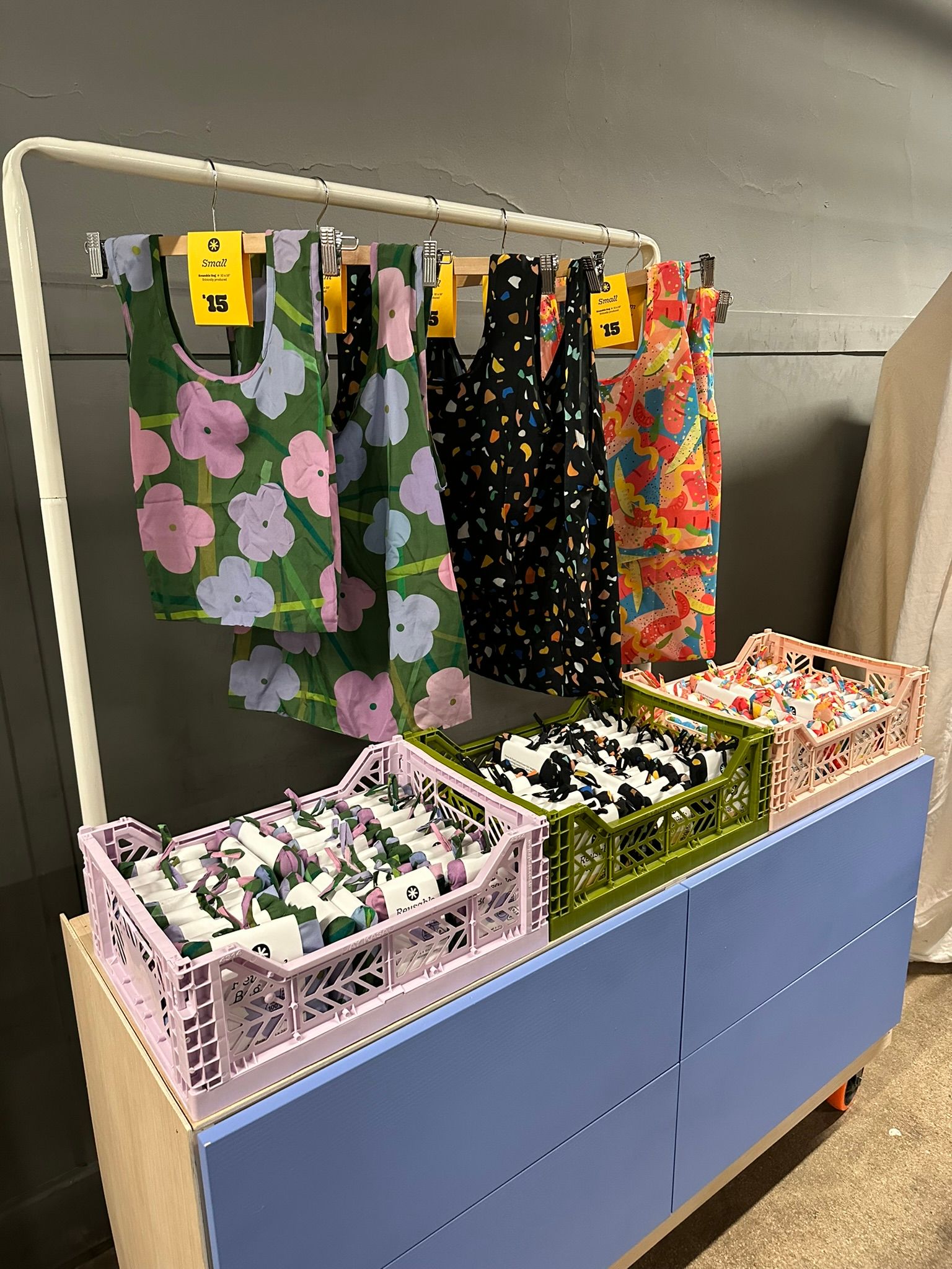 Retail display with colorful patterned fabrics hanging on rack above bins of folded textiles.