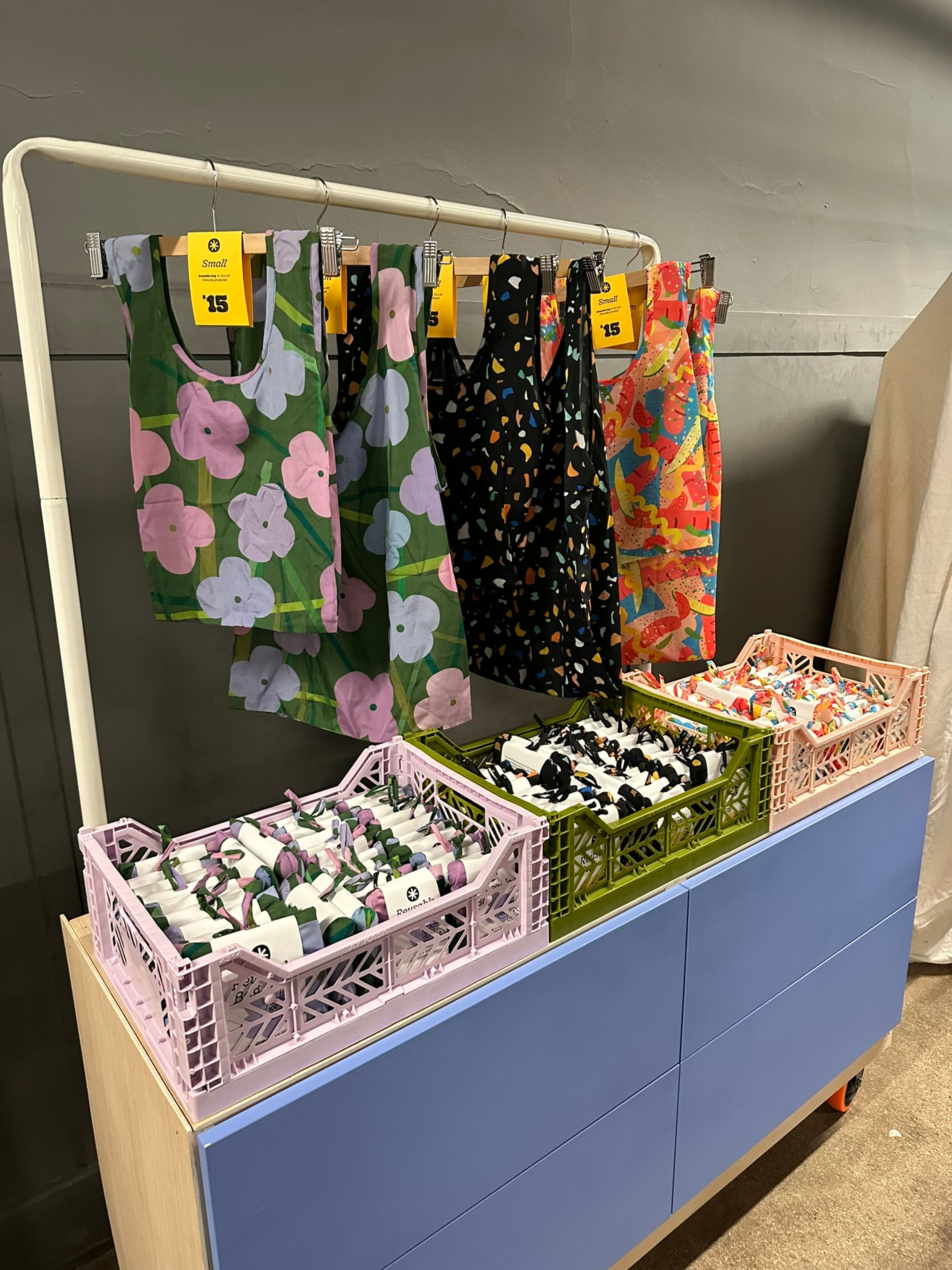 Retail display with colorful patterned fabrics hanging on rack above bins of folded textiles.