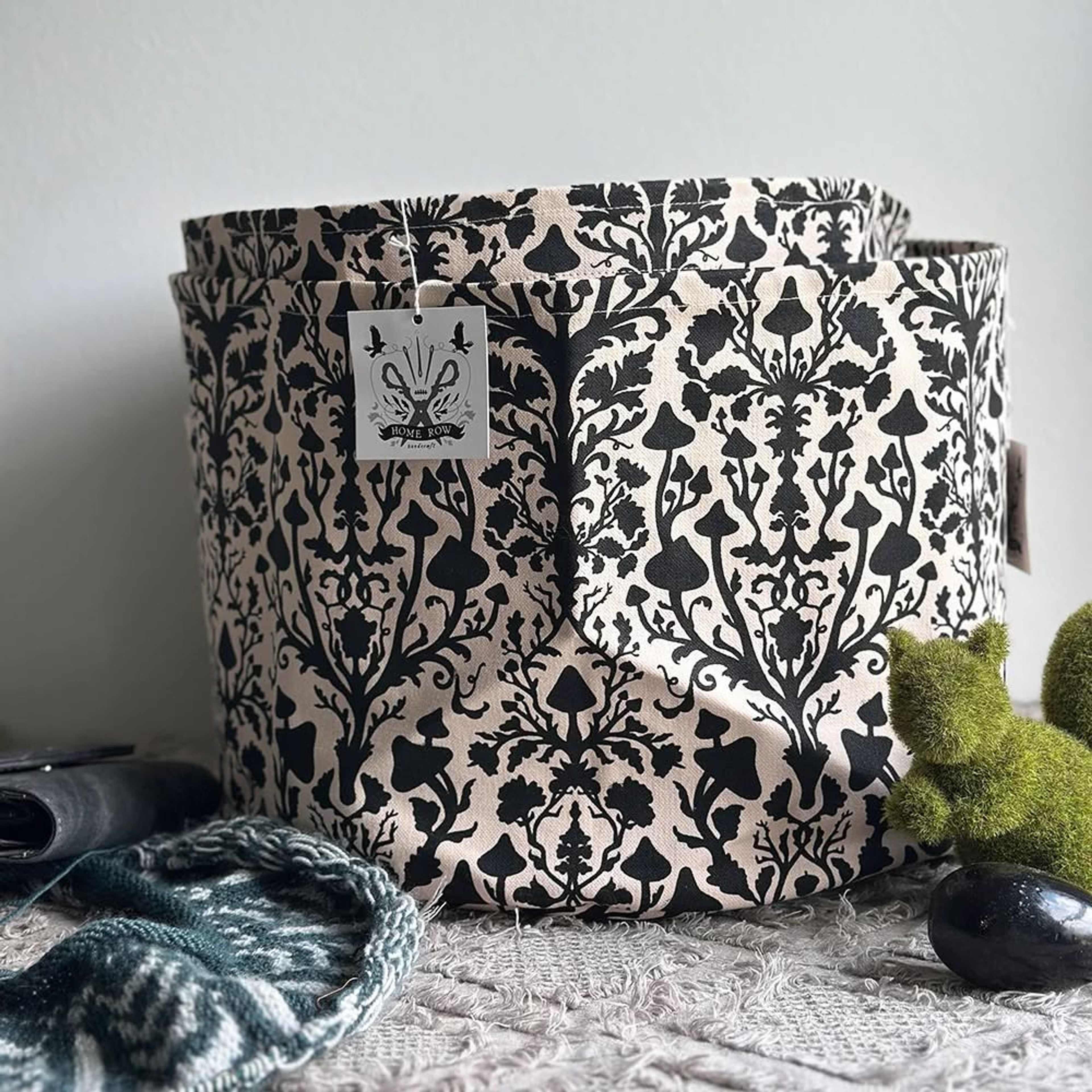 Decorative fabric storage basket with black damask pattern, label, and surrounding items.