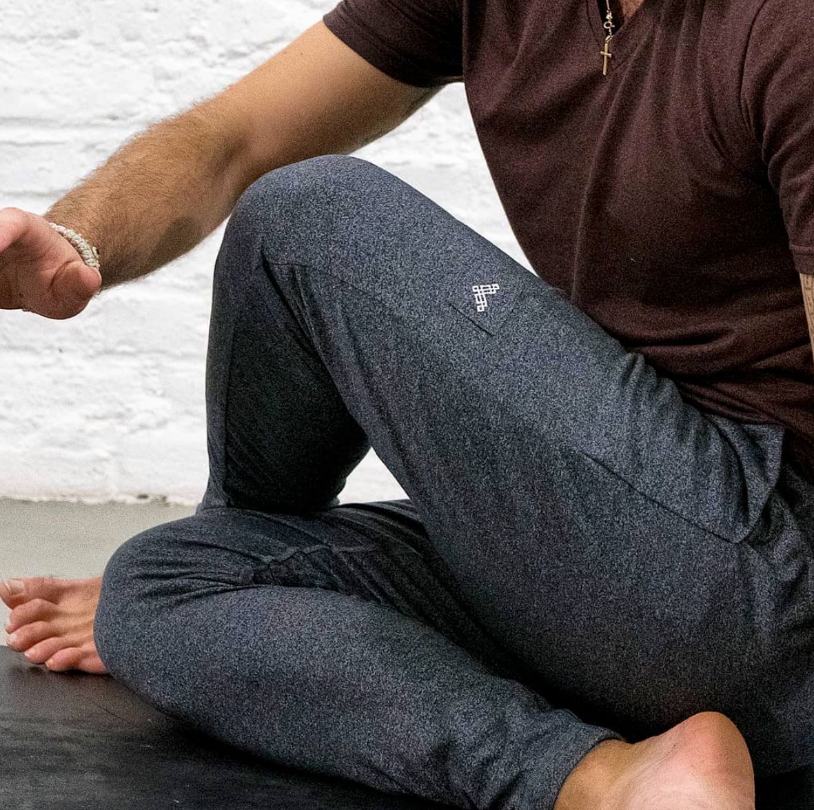 Man sitting on beach wearing dark gray sweatpants and brown t-shirt.