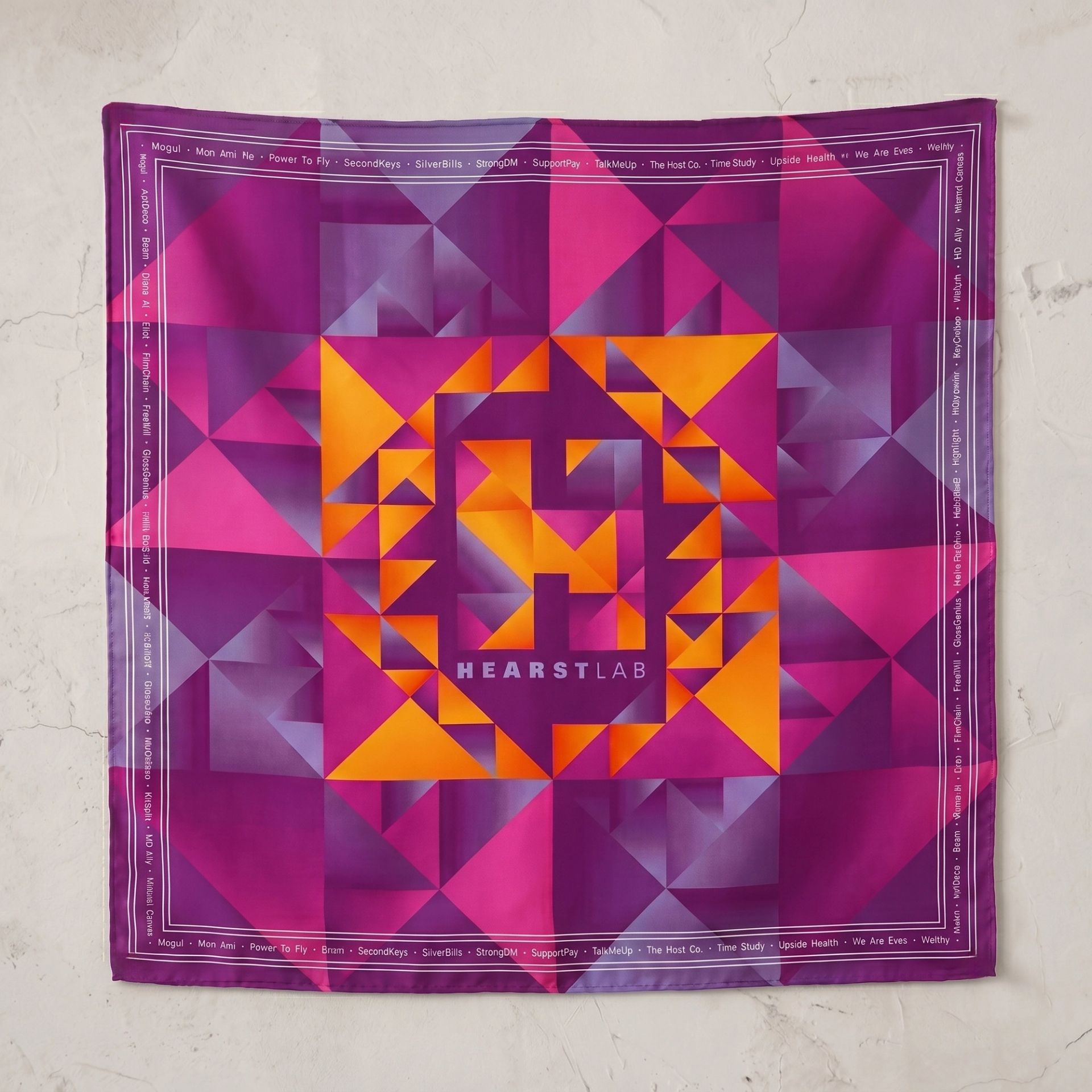 A custom-printed silk scarf featuring a vibrant geometric pattern in purple, magenta, and orange. The center displays the HearstLab logo, and the border includes a list of words.