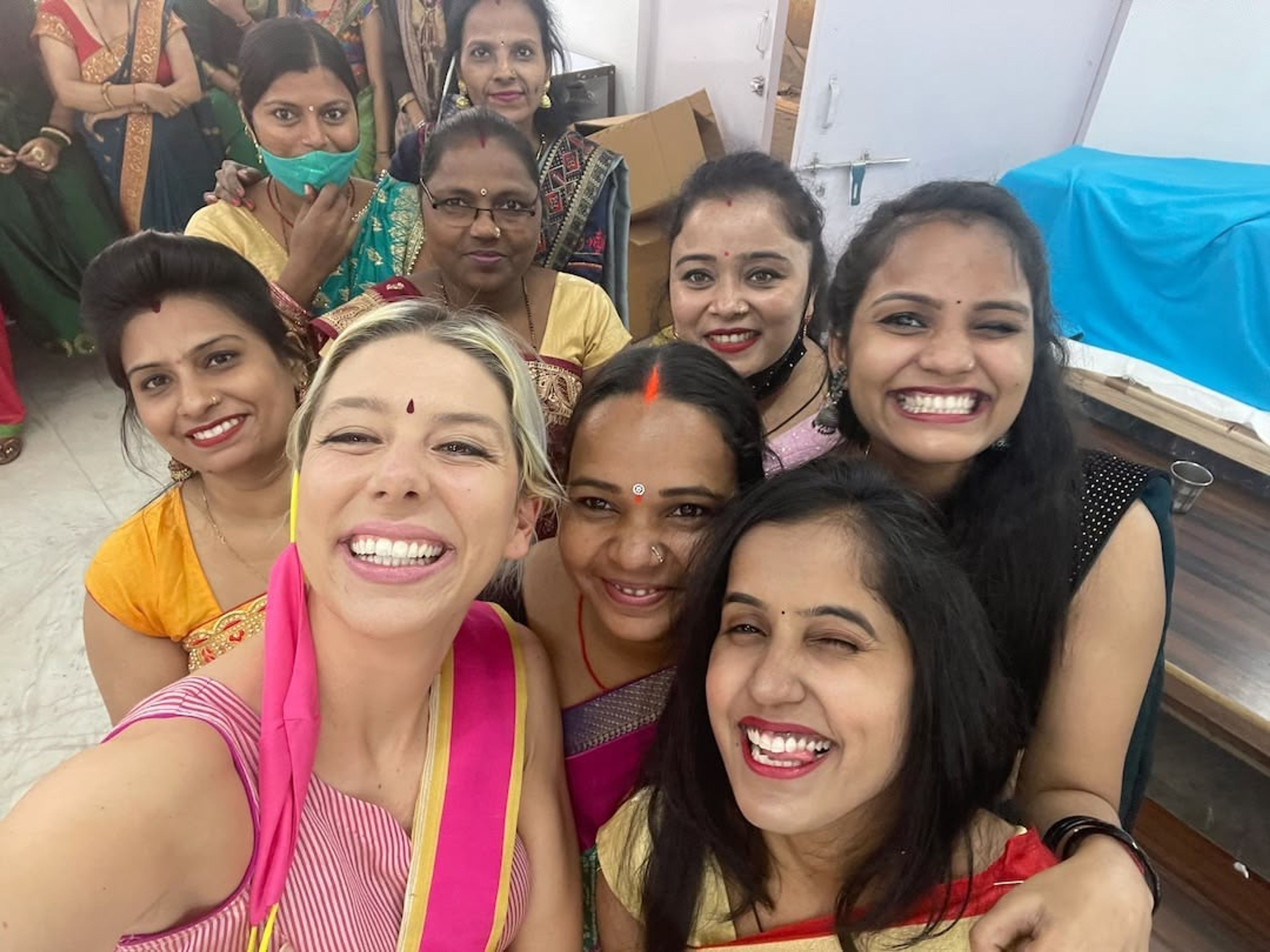 Group of women in traditional Indian attire smiling at camera indoors.