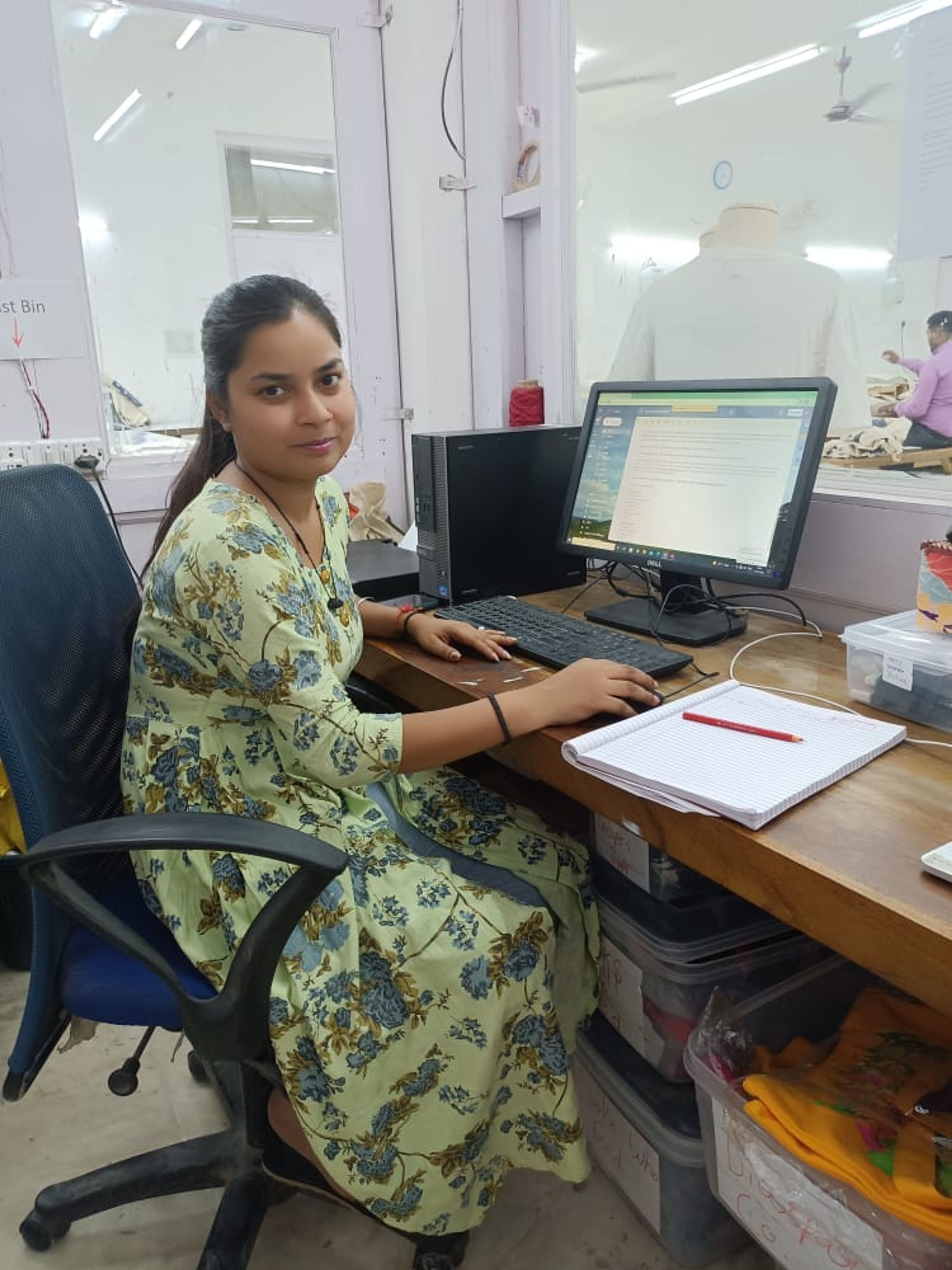 Woman in yellow floral dress working at computer desk in office workspace.
