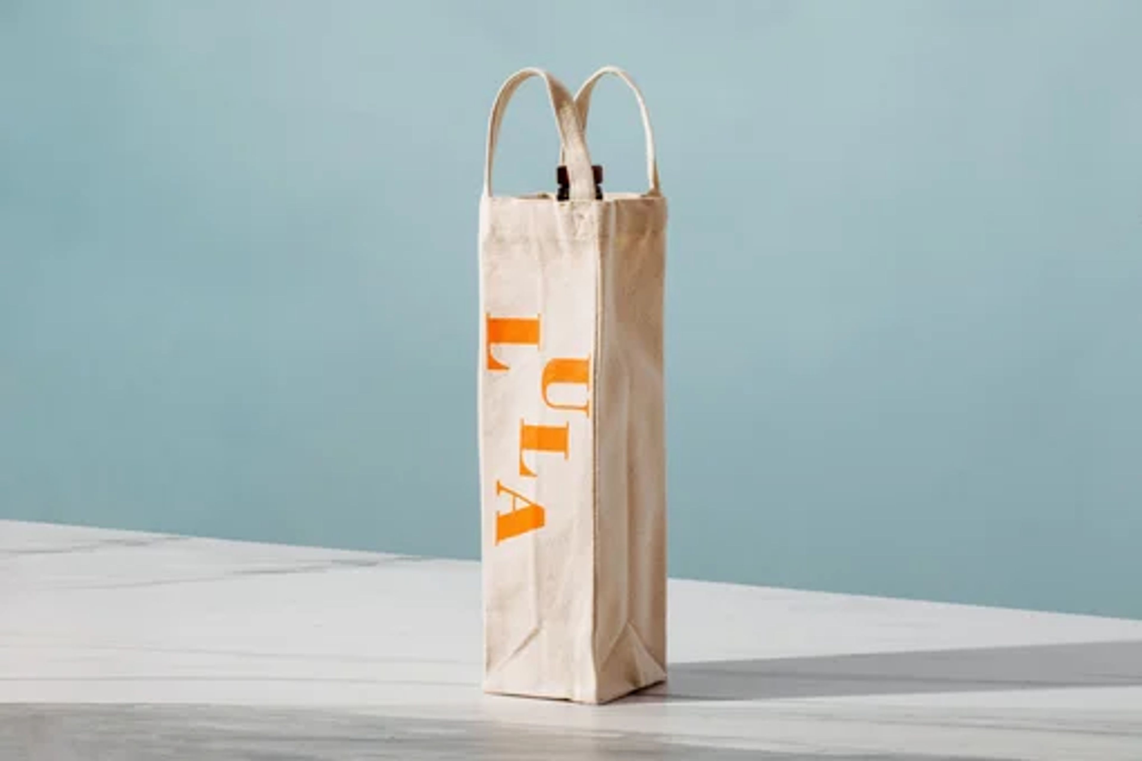 Canvas wine bottle bag with orange design on white surface against blue background.
