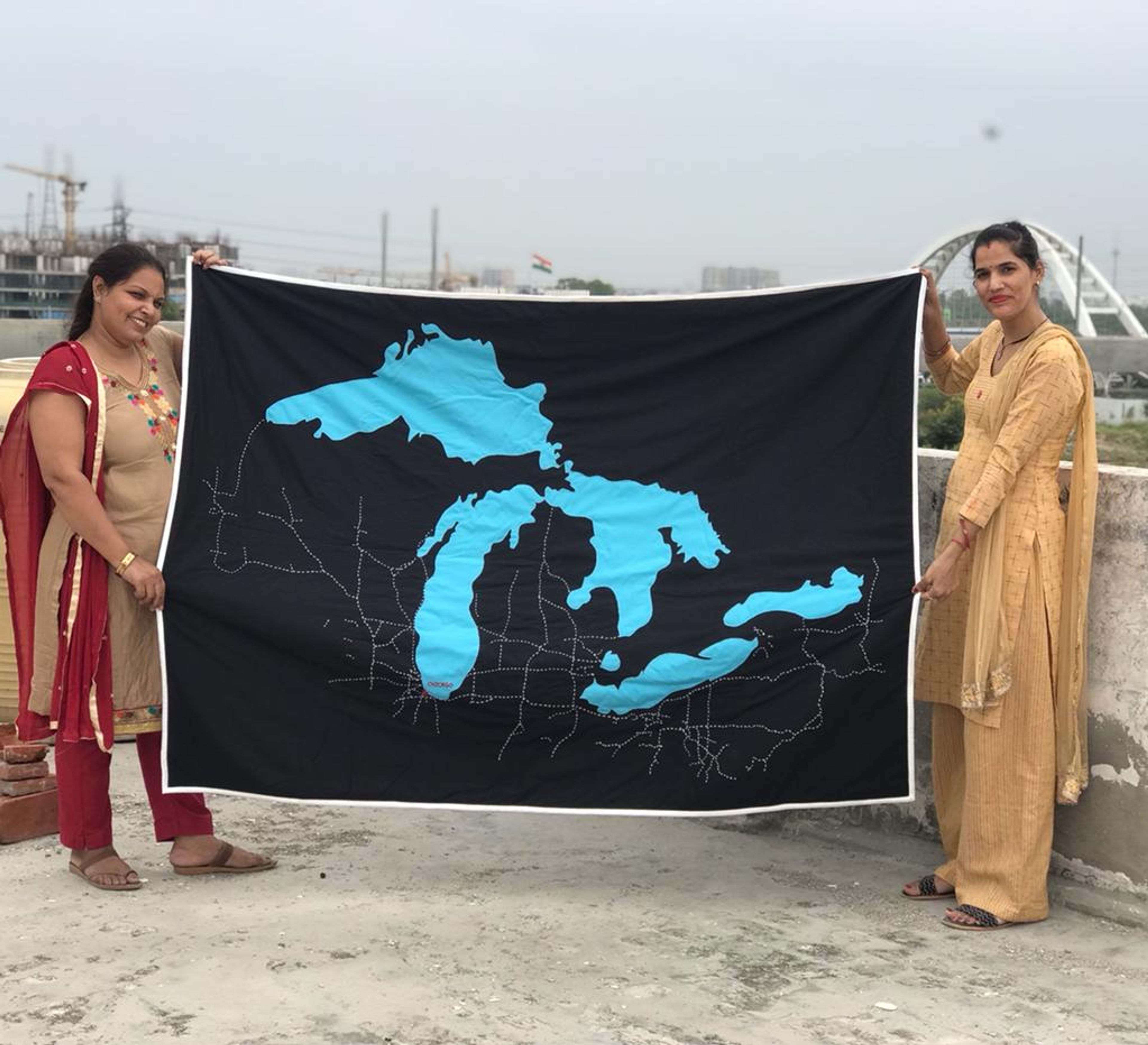 Two women holding banner displaying map of Great Lakes region on rooftop.