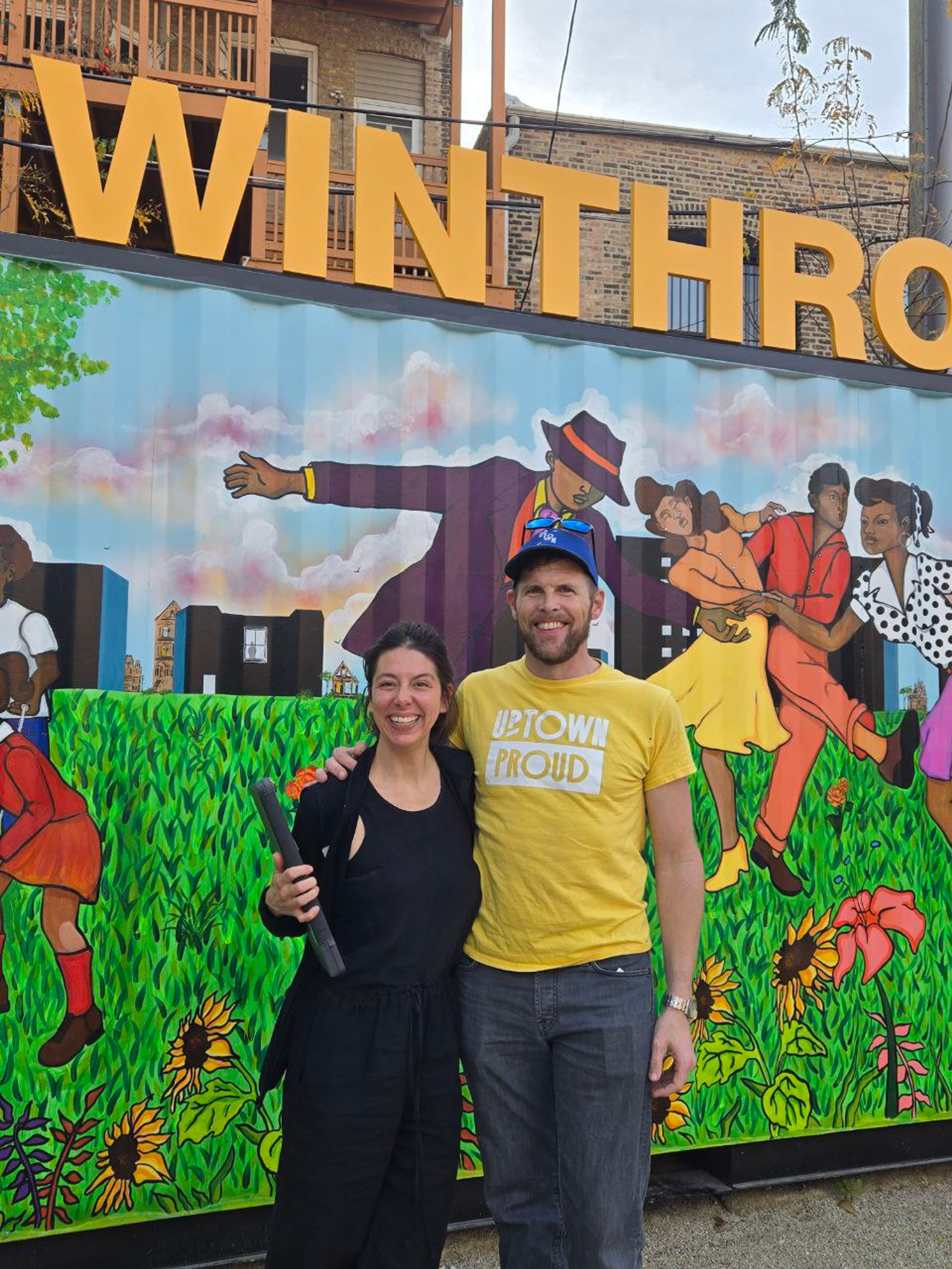 Two people posing in front of colorful "Winthrop" mural with vibrant artwork and yellow lettering.